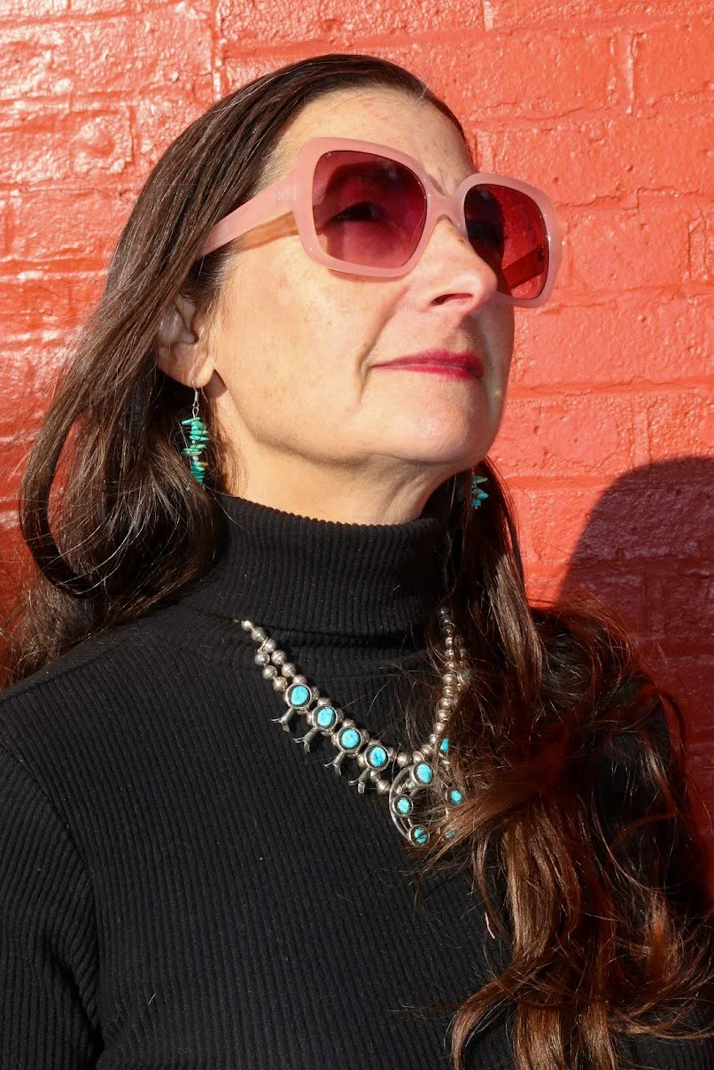 Customer wearing a Kingman turquoise squash blossom necklace and turquoise earrings against a brick wall in downtown Kingman, AZ