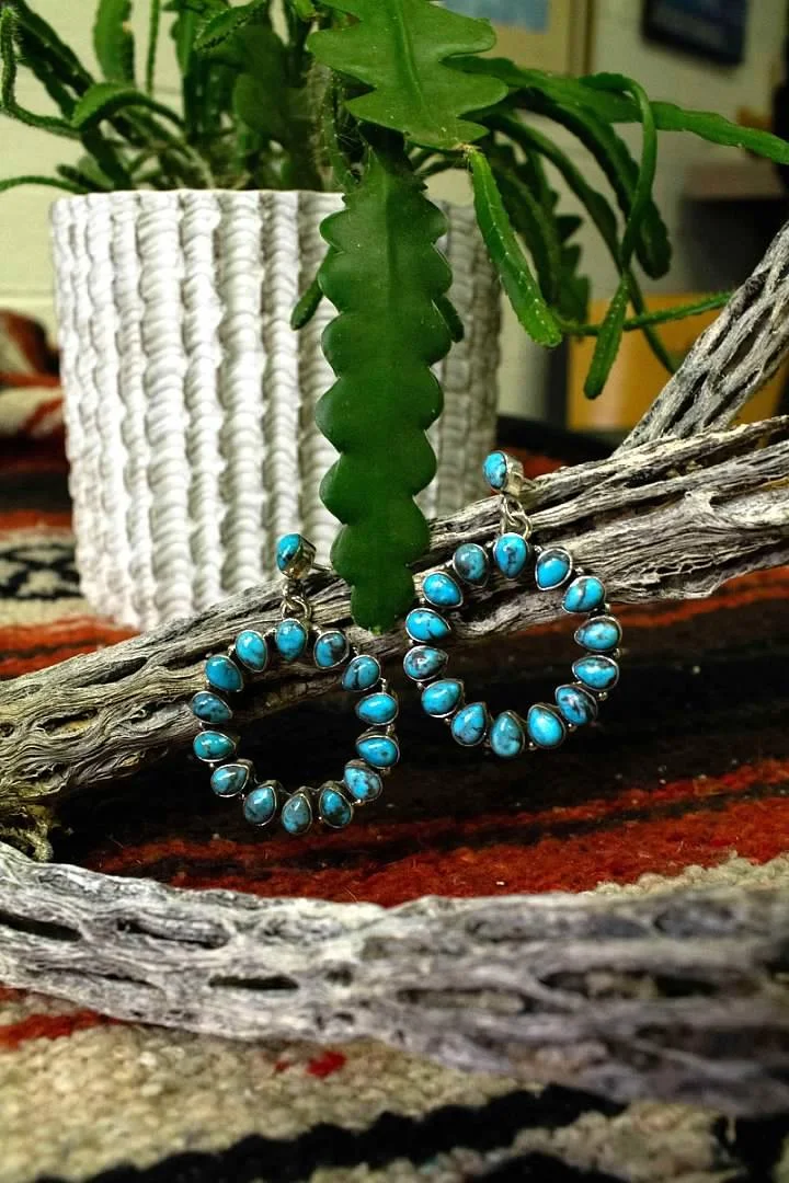 Kingman turquoise cluster hoop earrings in sterling silver, displayed on cholla wood over a Southwestern rug